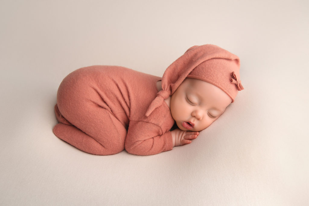 baby girl lays in orange outfit on studio prop 